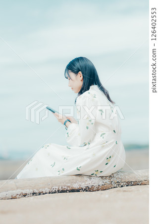 A woman in a floral dress looking at her smartphone on the beach 126402553
