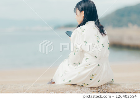 A woman in a floral dress looking at her smartphone on the beach A woman in a floral dress looking at her smartphone on the beach 126402554