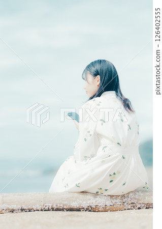 一位身穿花裙的女子在海灘上看著她的智慧型手機 126402555