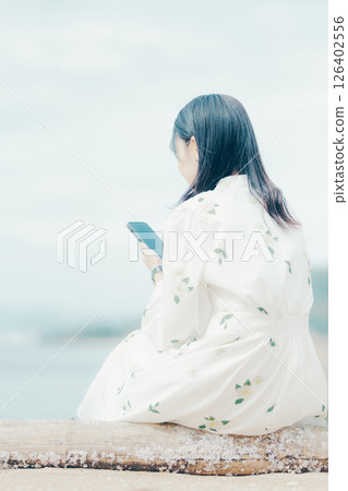 一位身穿花裙的女子在海灘上看著她的智慧型手機 126402556