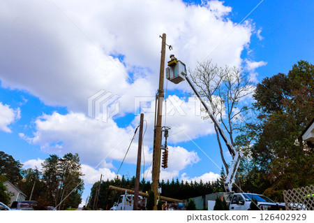Utility workers use lift trucks to repair power lines while ensuring safety in residential area during works day. 126402929
