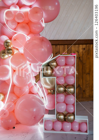 A stunning pink and rose gold balloon garland and number one backdrop for a first birthday celebration, featuring a marble floor and rustic wood paneling 126403196