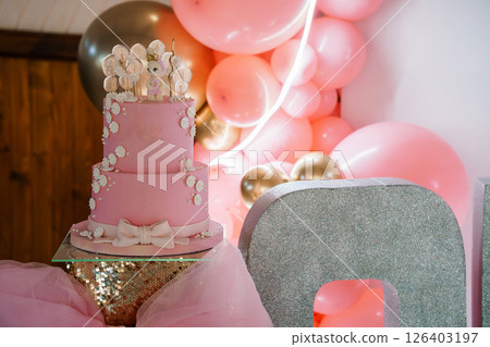 Adorable Two-Tiered Pink Baby Girl First Birthday Cake with Elephant Decorations in a Festive Balloon Backdrop Setting 126403197