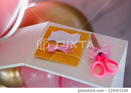 A close-up shot showcases a pink and gold themed gift presentation with a blank label, decorative scissors, and balloons, creating a festivity atmosphere A close-up shot showcases a pink and gold themed gift presentation with a blank label, decorative scissors, and balloons, creating a festivity atmosphere 126403199