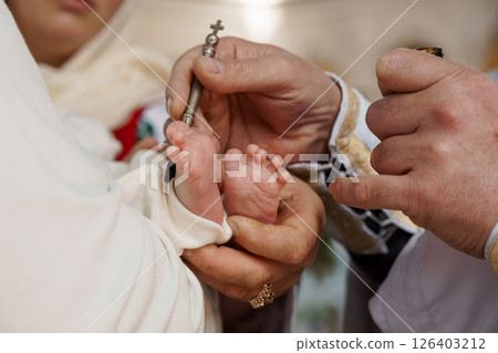 A tender religious moment capturing the sacrament of baptism as a priest carefully pours water over the foot of a baby during a church ceremony 126403212