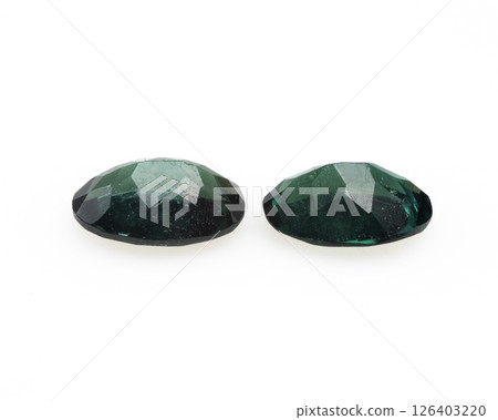 Two dark green chrome tourmaline gemstones displayed on a white surface, exhibiting oval cuts and faceted surfaces, providing a clear view of their natural inclusions and vibrant color Two dark green chrome tourmaline gemstones displayed on a white surface, exhibiting oval cuts and faceted surfaces, providing a clear view of their natural inclusions and vibrant color 126403220