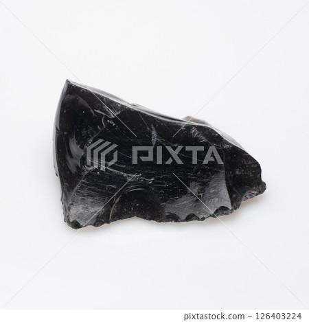 Polished Black Obsidian Fragment with Natural Textures and Iridescent Sheen, Showing Volcanic Glass Formations and Intricate Fracture Patterns on White Background 126403224