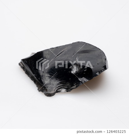 A highly polished black obsidian fragment displaying a sharp, glass-like surface and a distinctive conchoidal fracture pattern, exhibiting a smooth texture and a reflective sheen A highly polished black obsidian fragment displaying a sharp, glass-like surface and a distinctive conchoidal fracture pattern, exhibiting a smooth texture and a reflective sheen 126403225