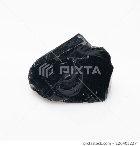 A close-up shot of a rough, black obsidian rock fragment displaying a glossy, reflective surface with swirling patterns and a sharp, fractured edge against a plain white background A close-up shot of a rough, black obsidian rock fragment displaying a glossy, reflective surface with swirling patterns and a sharp, fractured edge against a plain white background 126403227