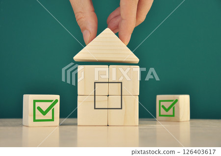 Businessman builds a mini house from wooden blocks. 126403617