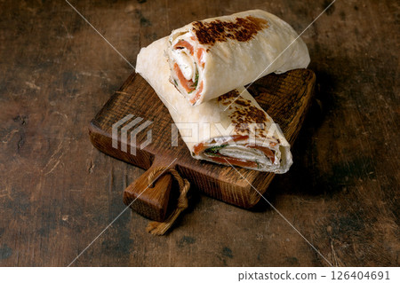 Fresh salmon tortilla wraps with cream cheese herbs on vintage wooden cutting board. Homemade appetizer on rustic table background. 126404691
