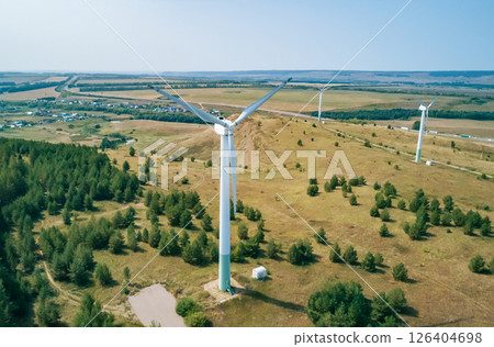 Tall wind turbines rise above rolling hills and a lush green forest, showcasing renewable energy efforts. Tall wind turbines rise above rolling hills and a lush green forest, showcasing renewable energy efforts. 126404698
