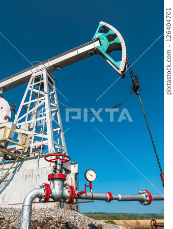 A large oil pump jack operates in an open field, extracting crude oil 126404701