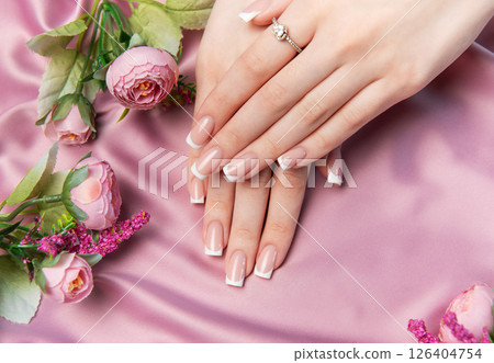 Woman showing french manicure on pink satin background with flowers 126404754