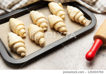 Raw croissants baking on tray with rolling pin and kitchen towel 126404760