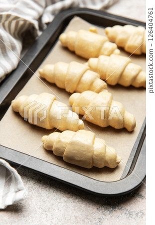 Raw croissants waiting to be baked on baking sheet with baking paper 126404761