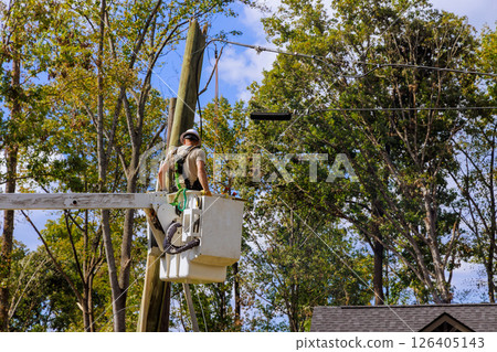 Utility worker stands in bucket lift fixing electrical lines above neighborhood with after hurricane 126405143