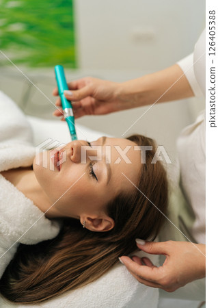Vertical shot of professional beautician performing microneedling treatment with dermapen on female patient forehead, targeting skin rejuvenation enhancing collagen production, close-up, slow motion Vertical shot of professional beautician performing microneedling treatment with dermapen on female patient forehead, targeting skin rejuvenation enhancing collagen production, close-up, slow motion 126405388