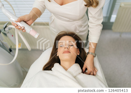 Top view of unrecognizable beautician performing mesotherapy treatment with specialized device on woman facial skin, targeting skin rejuvenation and age-defying results in aesthetic clinic. 126405413
