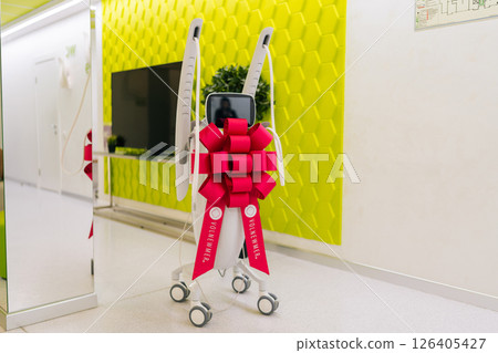 Modern mesotherapy machine with festive bow in corridor of new beauty clinic or medical center, symbolizing innovation in skincare, aesthetic medicine, nobody. Concept of beauty treatment. Modern mesotherapy machine with festive bow in corridor of new beauty clinic or medical center, symbolizing innovation in skincare, aesthetic medicine, nobody. Concept of beauty treatment. 126405427