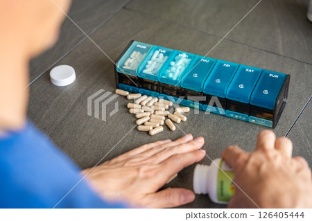 Man sorting his pills and supplements into a weekly pill organizer. Concept of medication management and daily health routine Man sorting his pills and supplements into a weekly pill organizer. Concept of medication management and daily health routine 126405444