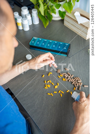 Man sorting his pills and supplements into a weekly pill organizer. Concept of medication management and daily health routine 126405445