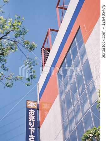 一張膠片照片，顯示街道樹木的新鮮綠意，以及一家大型二手商品商店的外觀，上面掛著“把你的書賣給我們”的牌子。 126405478