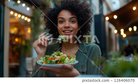 Young woman enjoying a fresh salad outdoors in a cozy setting. 126406070