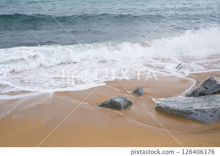 Waves crashing on sandy beach with rocks and clear sky Waves crashing on sandy beach with rocks and clear sky 126406176