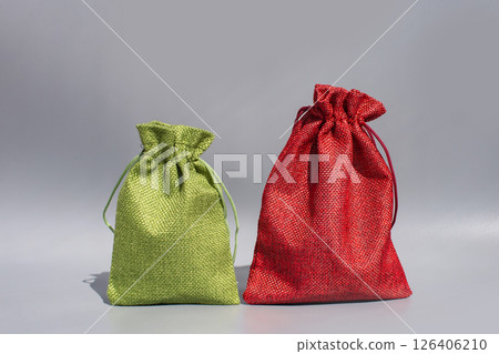 Green and red drawstring fabric pouches on gray background 126406210