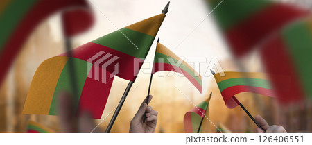 Lithuania flags in their hands on a blurred urban background Lithuania flags in their hands on a blurred urban background 126406551