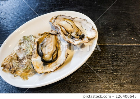 Close up of grilled raw oyster in three pieces on a white plate with copy space  126406643