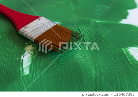 A bright red brush rests on rich green paint in an artist's studio 126407392