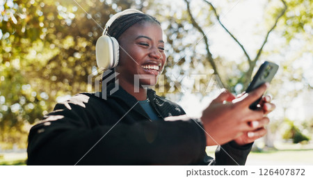 Park, athlete and woman with smartphone, headphones and tracking progress of exercise on app and smile. Outdoor, browsing and black person with mobile for social media, online and listening to music 126407872