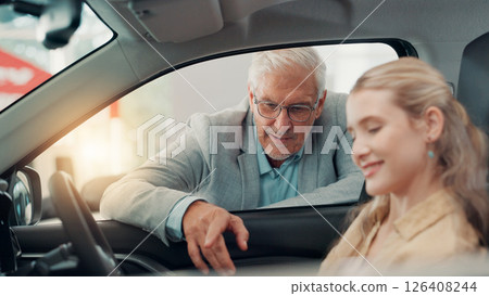 Drive, customer and salesman with talking in car dealership, transport model and rental service. Showroom, woman and mature seller with pitch for vehicle features, assistance and discussion by flare 126408244