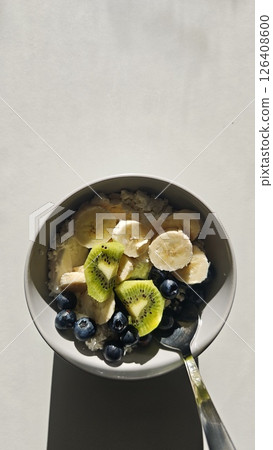 Bowl of cottage cheese with banana, kiwi, and blueberries served with a spoon on a light background. Concept of healthy breakfast, natural nutrition, and balanced eating Bowl of cottage cheese with banana, kiwi, and blueberries served with a spoon on a light background. Concept of healthy breakfast, natural nutrition, and balanced eating 126408600