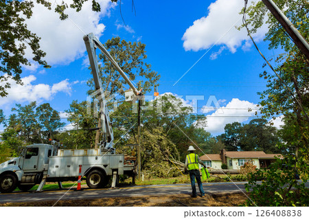 Workers operate bucket truck to repairs power lines in suburban neighborhood after storm. 126408838