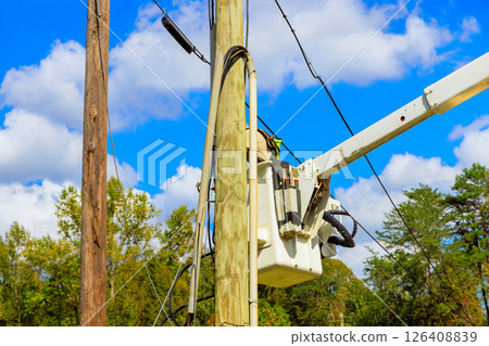 Workers use crane truck from bucket lift to conduct maintenance on power lines against backdrop after hurricane 126408839