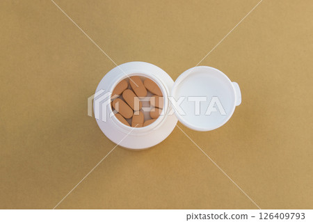 Pills in white open bottle on the yellow nature background. Farmacy concept. Top view. Space for text. 126409793