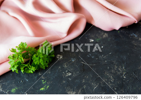 Pink gentle silk fabric and green spring herbs on the rough black texture background. 126409796