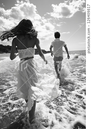 Romantic beach scene with man and woman running into the sea, captured in black and white 126409817