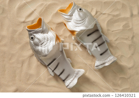 Rubber slippers shaped of fish. Fishermen slippers for beach on sand. Summer beach vacation. Creative funny flip flops. View from above. Rubber slippers shaped of fish. Fishermen slippers for beach on sand. Summer beach vacation. Creative funny flip flops. View from above. 126410321