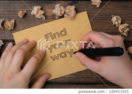 A hand is writing on a piece of paper that says find your way. The paper is on 126411501