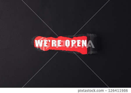 A red and black sign that says We're open is shown with a tear in it 126411986
