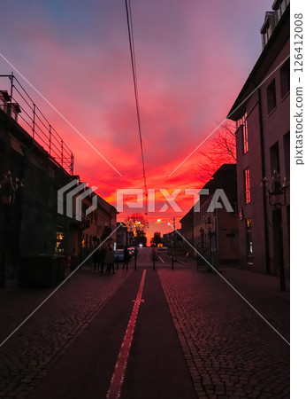 A street with a red sky and a few people walking down it 126412008