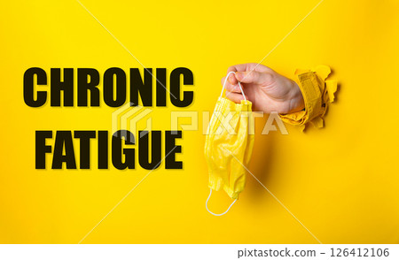 Person holding a yellow mask with the words Chronic Fatigue written below Person holding a yellow mask with the words Chronic Fatigue written below 126412106
