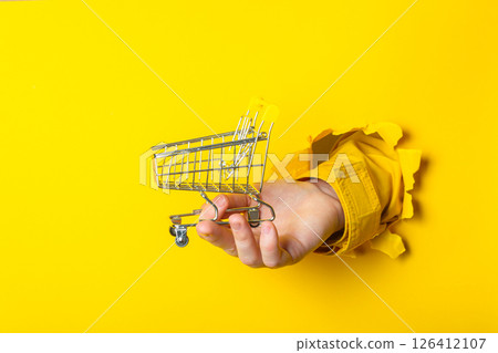 Hand holding a shopping cart in a yellow background Hand holding a shopping cart in a yellow background 126412107