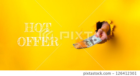 Person is holding a bill in a hole in a yellow background 126412301