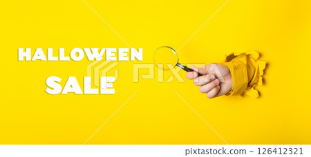 A hand holding a magnifying glass with the words Halloween Sale written below it A hand holding a magnifying glass with the words Halloween Sale written below it 126412321
