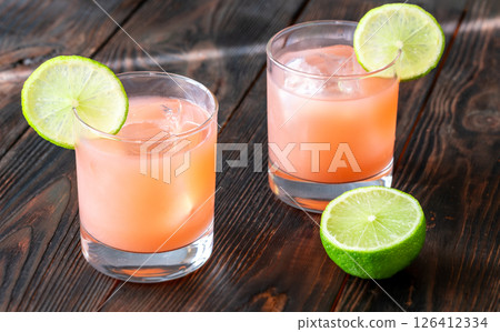 Two guava margaritas with lime wheels glow against rich dark cocktail backdrop 126412334